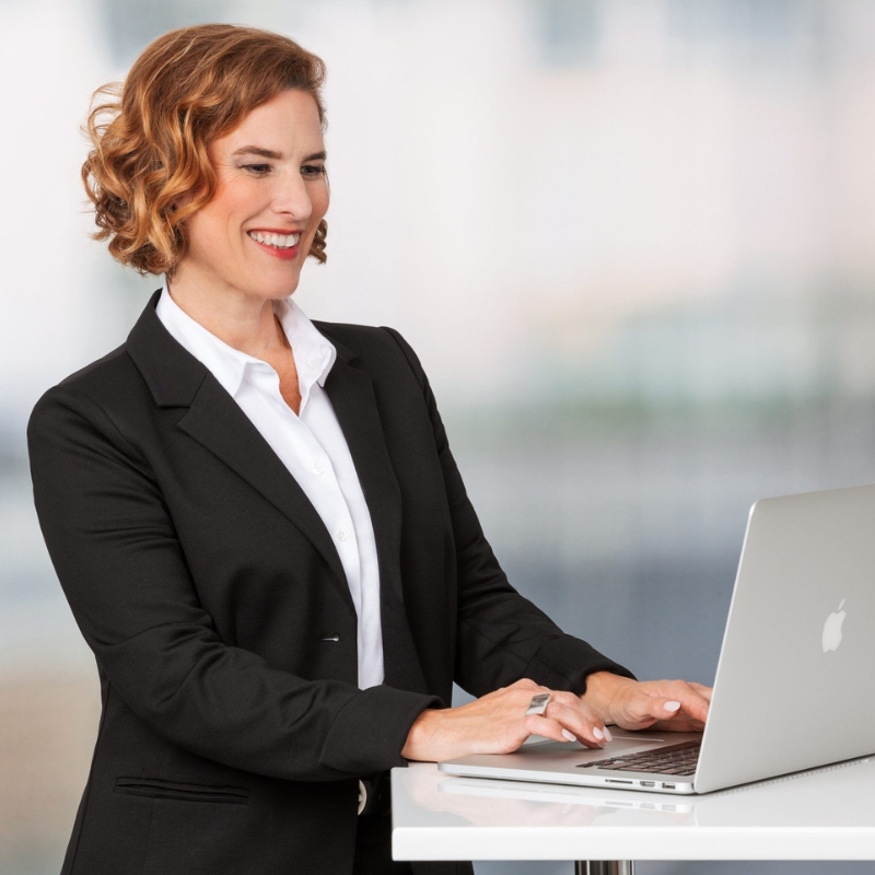 Isabelle Mall, Stressmanagement Akademie, arbeitet lächelnd am Laptop und bereitet Stressmanagement Seminar online vor